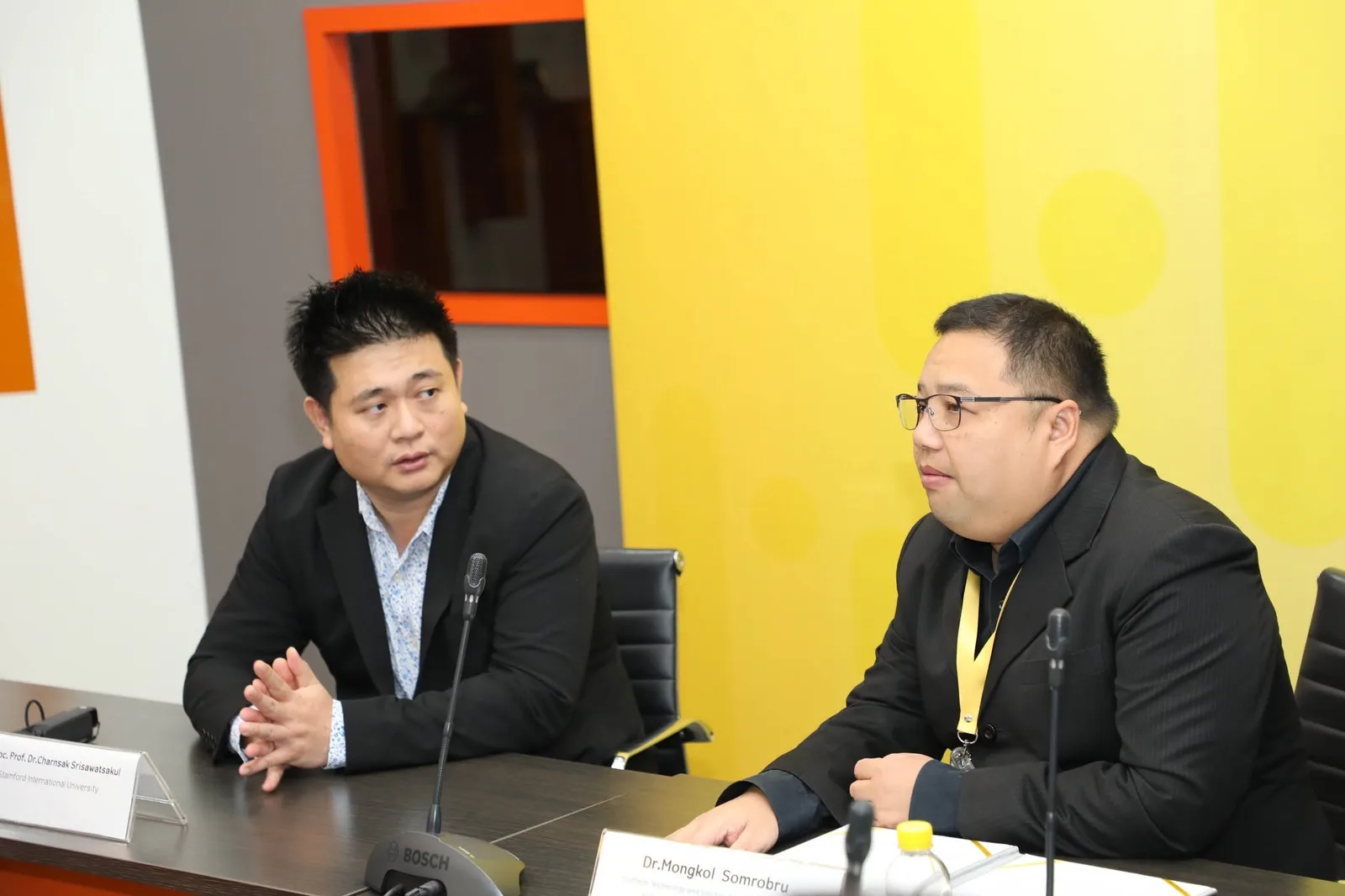 Charnsak Srisawatsakul and a National Telecom representative sit at microphones during an industry discussion